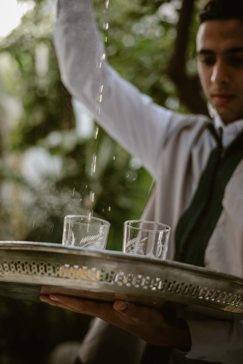 Traditional Moroccon tea being served in a natural environment with plants and leaves in the background.